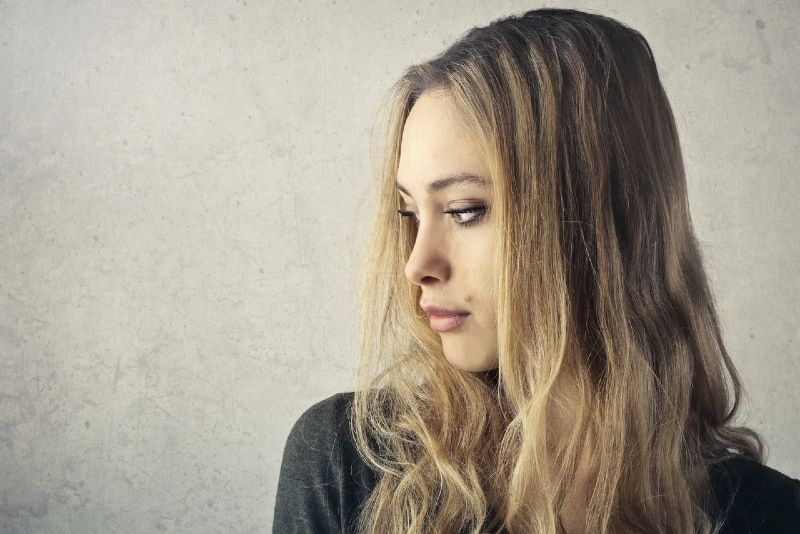 blonde vrouw in grijze top die bij de muur staat