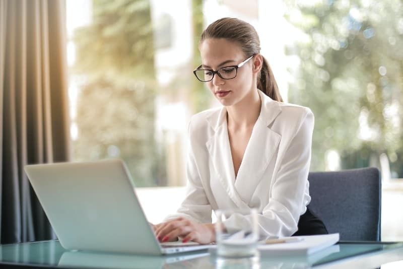 vrouw met bril die aan tafel zit en laptop gebruikt