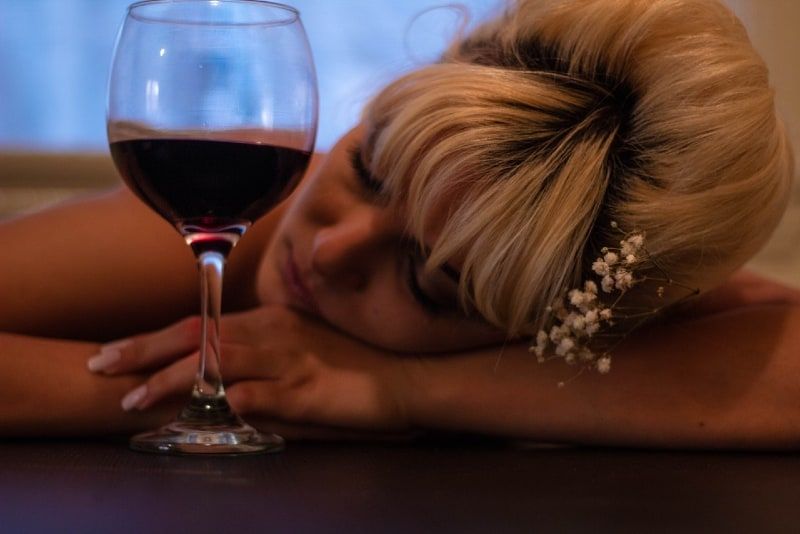 vrouw leunt met haar hoofd op tafel naast halfgevuld wijnglas