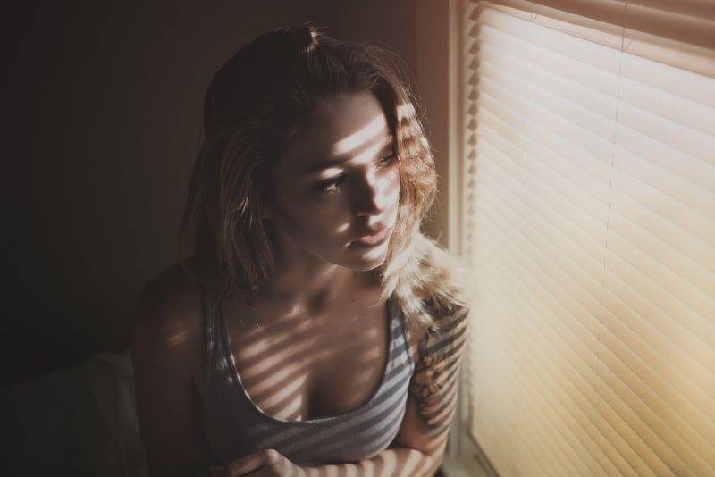 vrouw in grijze top die door jaloezieën kijkt