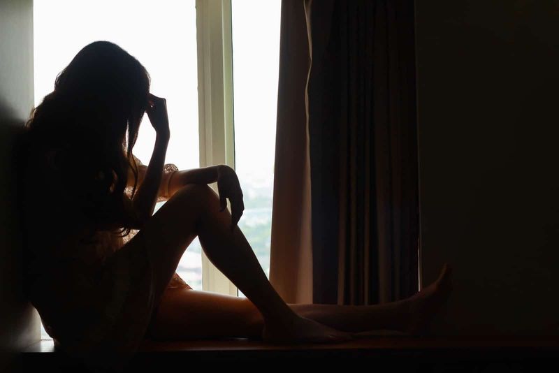 een depressieve vrouw zit bij het raam en lijdt