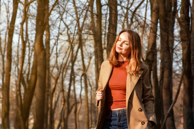 Eine lächelnde Brünette im Wald steht in einem braunen Mantel auf