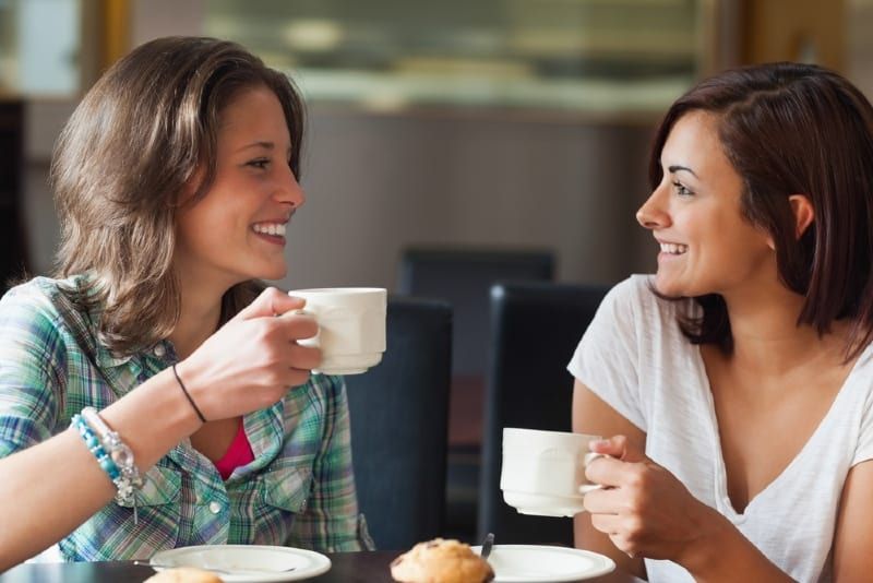 hai người phụ nữ cầm cốc trắng và nói chuyện