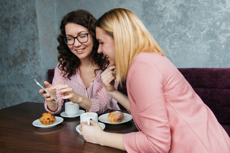 hai người phụ nữ nhìn vào điện thoại thông minh khi ngồi trên bàn