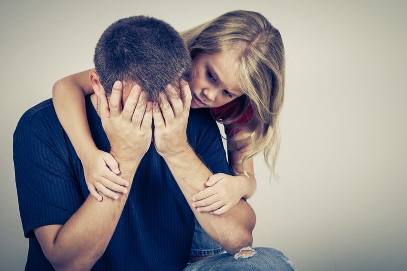 Trauriger Vater, getröstet von seiner Tochter, die ihn umarmt