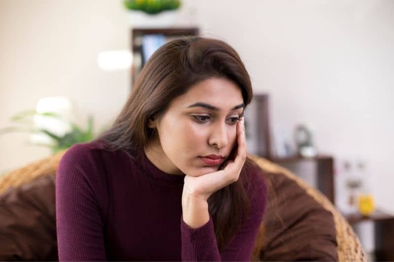 Traurige junge Frau, die auf einer braunen Couch im Wohnzimmer sitzt