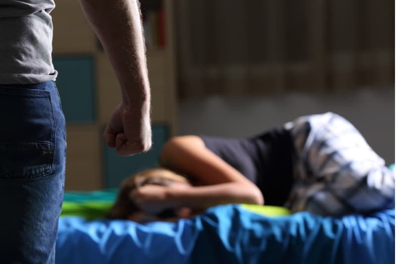 Misshandeltes Opfer, das auf dem Bett liegt, während ein beschnittener Mann mit enger Faust steht