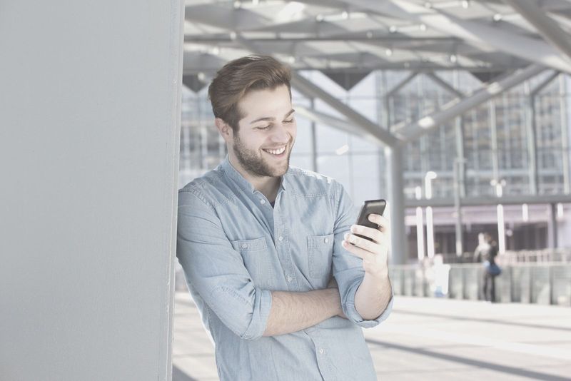 lächelnder Mann, der Textnachrichten von seinem Telefon vor einem Geschäft liest