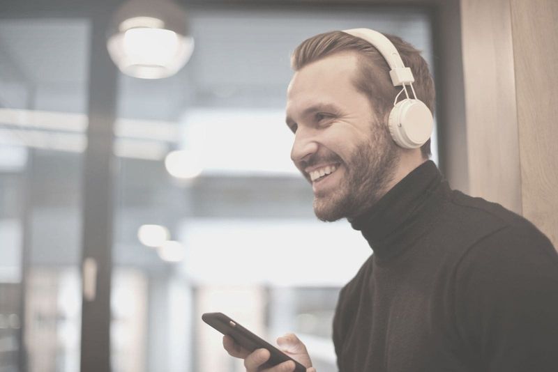 Mann mit einem Kopfhörer, der lächelt und drinnen ein Telefon hält