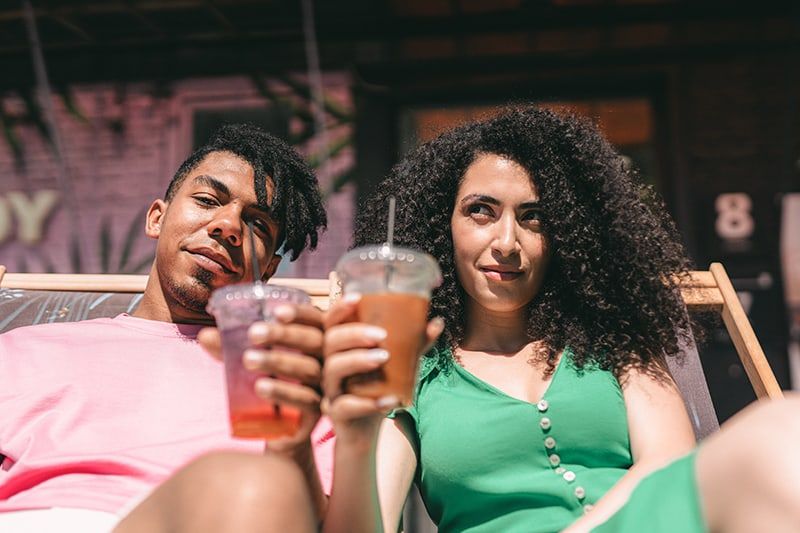 homem e mulher segurando bebidas enquanto estava deitado na espreguiçadeira