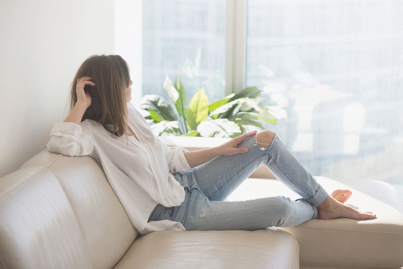 mujer pensativa relajada sentada en el sofá mirando fuera de las ventanas