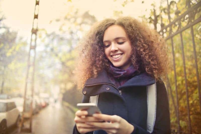 szczęśliwa dziewczyna patrząca na swój telefon na zewnątrz