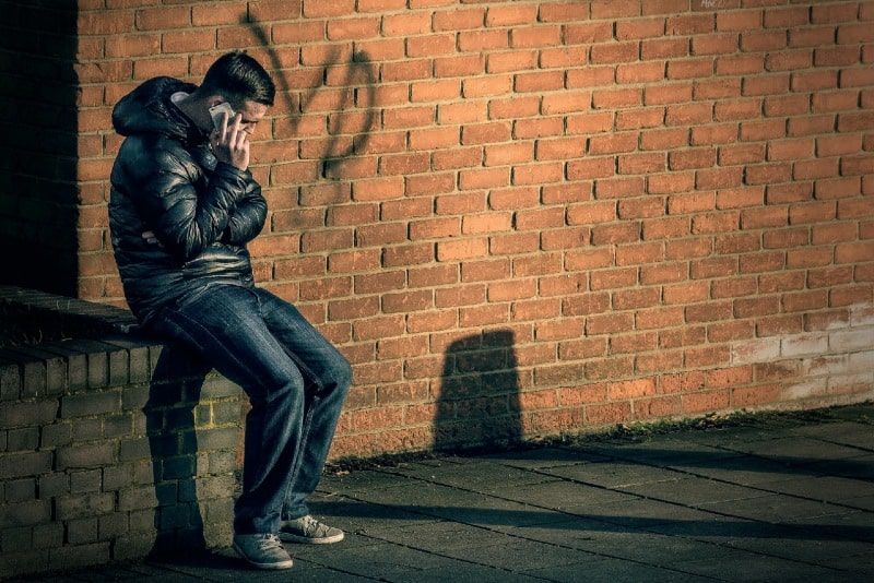 mężczyzna rozmawia przez telefon, siedząc na ceglanym murze