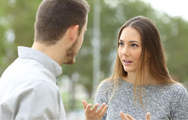امرأة تتجادل مع رجل يرفع يديها واقفًا في الهواء الطلق