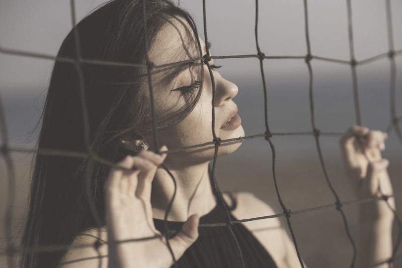 žena zatvara oči dok je blizu i drži na mreži u crnoj haljini na fotografiji izbliza