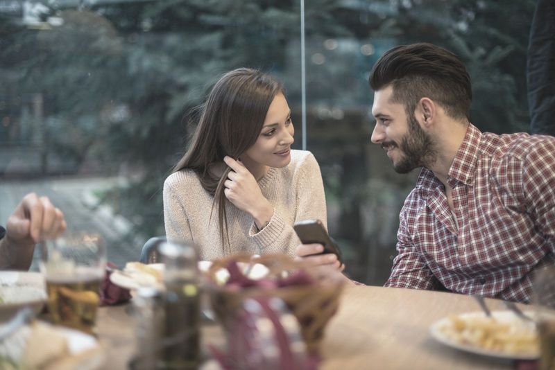 muškarac koji drži telefon dok sjedi pored žene u restoranu