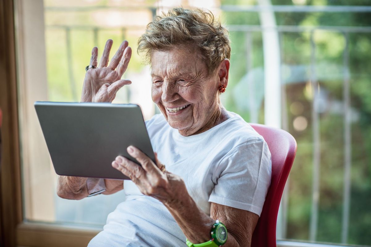 Uma mulher muito idosa usando um tablet digital na varanda do apartamento