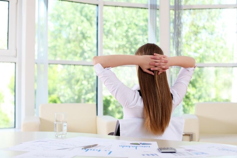 pengusaha wanita bersantai di kantor selama waktu istirahat menghadap jendela kantor