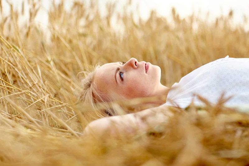 Eine blonde Frau liegt in einem Weizenfeld und blickt in den Himmel