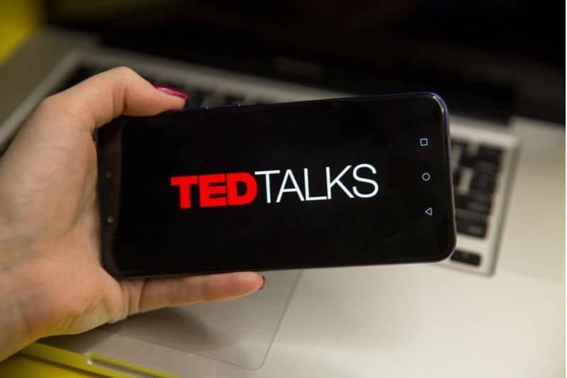 Logo ted talks wyświetlane na smartfonie trzymanym przez przyciętą kobietę