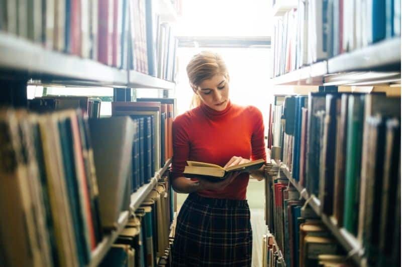 kobieta czytająca w bibliotece stojąca pośrodku półek z książkami