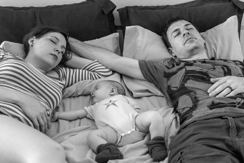 pais e bebê dormindo na cama