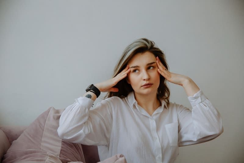 donna che ha mal di testa che si tocca la testa indossando maniche lunghe bianche