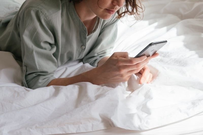 wanita menggunakan smartphone sambil berbaring di tempat tidur