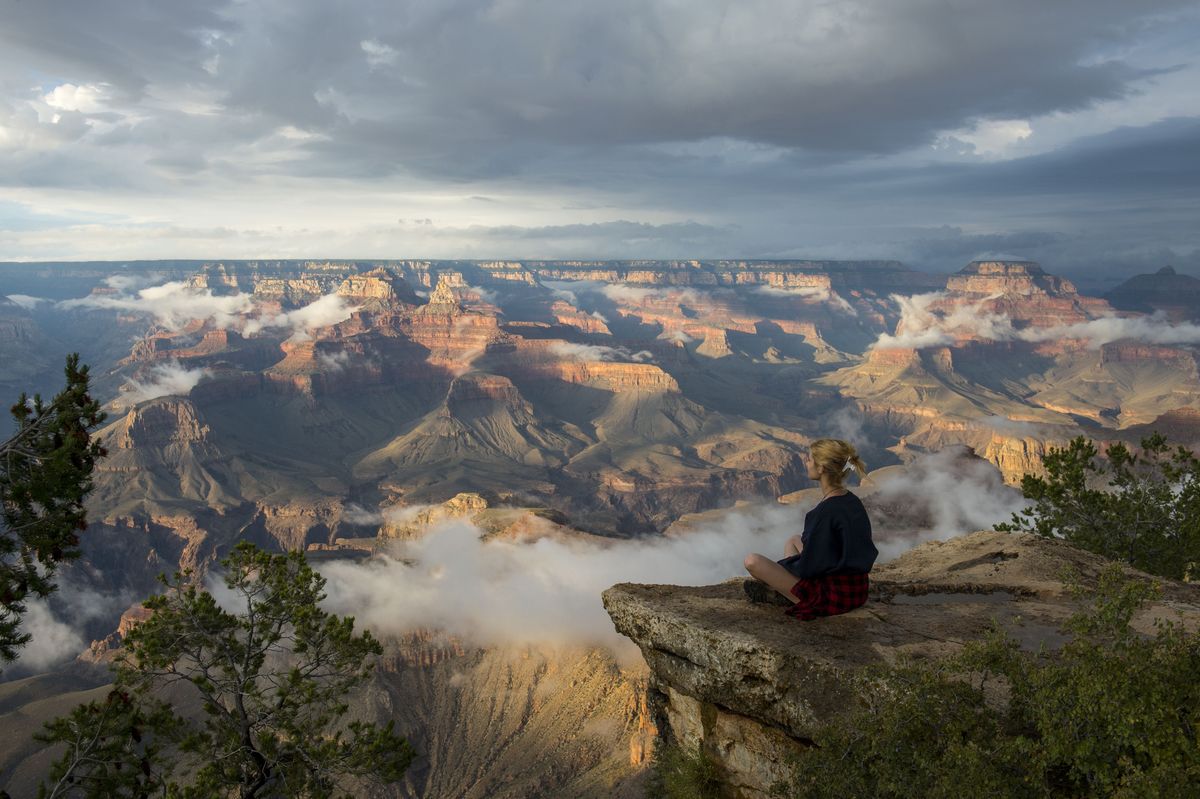 Eine junge Frau sitzt auf einem Felsen in der Nähe von Yavapai Point am ...