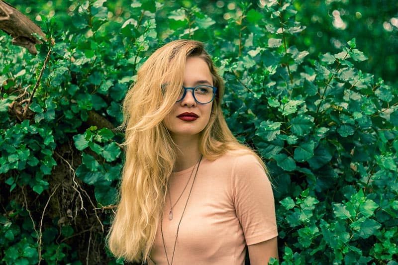 Vrouw met blauwe bril die voor de plantenmuur staat