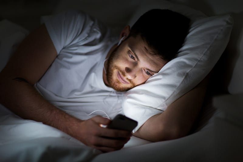 Man in bed met koptelefoon op en smartphone
