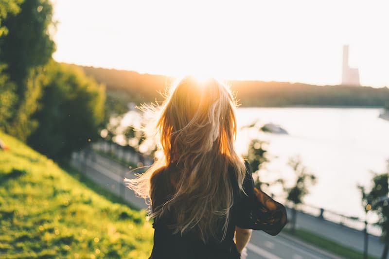 Achterkant van de vrouw die zit terwijl ze naar de zonsondergang kijkt