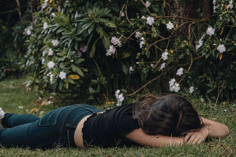 vrouw liggend op het gras in de buurt van bloemenstruik