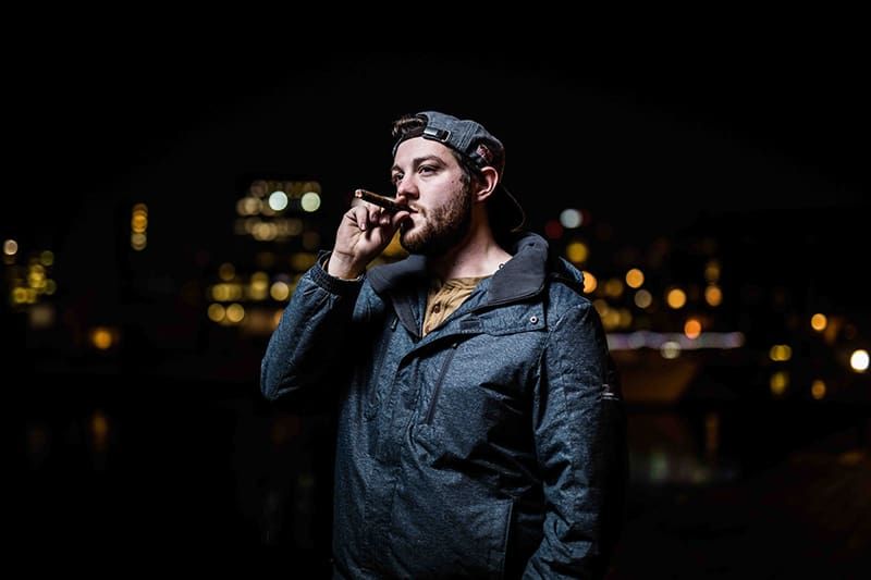 man in zwarte jas die staat terwijl hij sigaar rookt