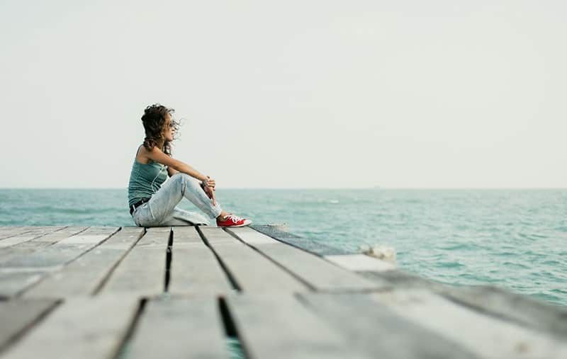 Frau am Meer sitzt auf einer Holzplattform