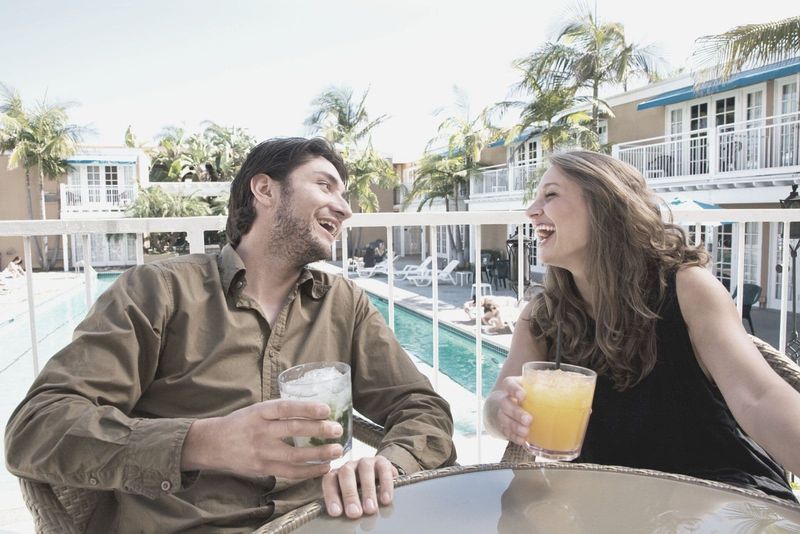 casal feliz rindo curtindo um ao outro ao lado da piscina bebendo bebida pela mesa