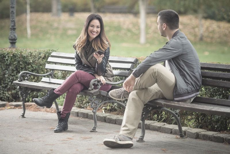 mulher feliz sorrindo para o cara sentado perto dela no banco do parque
