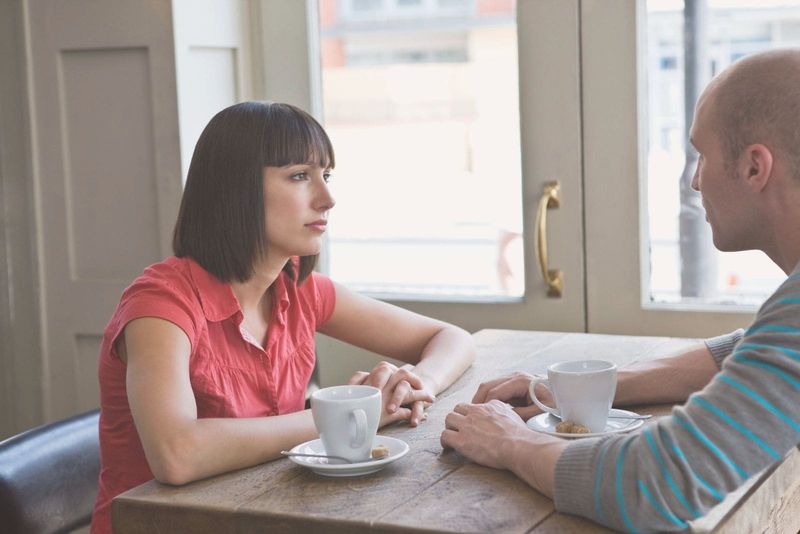 casal conversando no café seriamente sentado perto das janelas