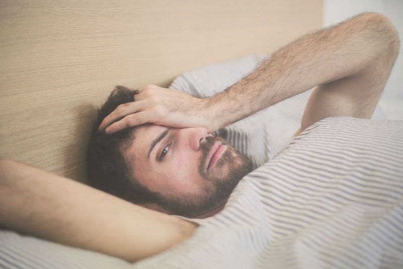 homem pensativo, deitado na cama e cobrindo o olho com uma mão