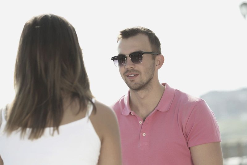 jovem vestindo camisa polo rosa e óculos de sol enquanto enfrenta e conversa com uma mulher ao ar livre