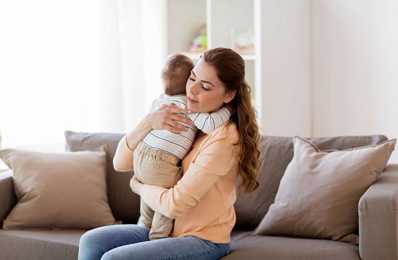 ibu muda yang bahagia memeluk anaknya sambil duduk di sofa
