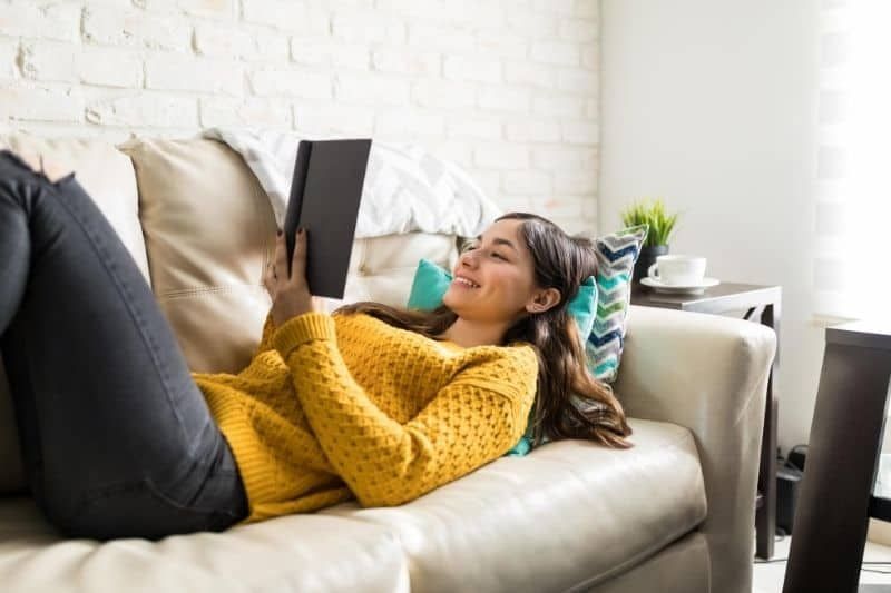 امرأة تقرأ كتابًا ملقاة على الأريكة داخل المنزل