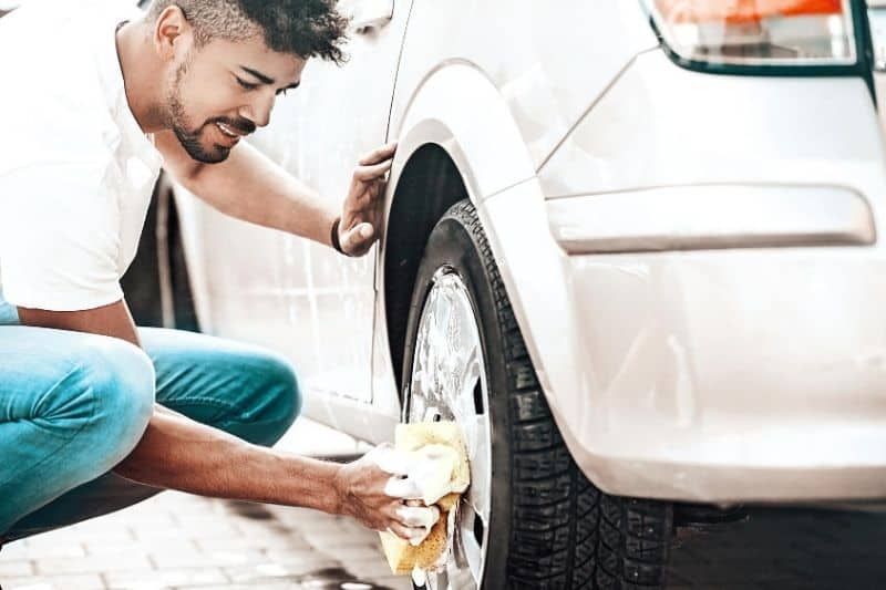 رجل ينظف إطارات السيارة بالإسفنج والصابون
