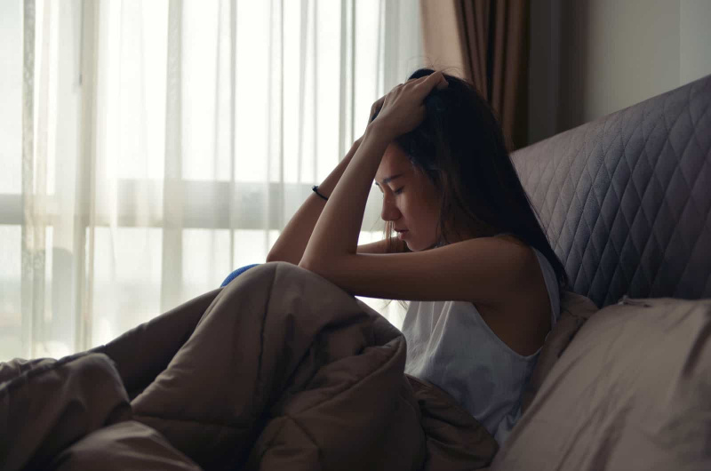 sehr traurige frau, die auf ihrem bett sitzt