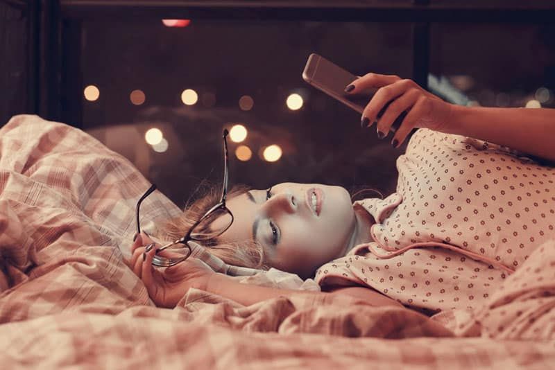 mooie jonge vrouw liggend op bed en kijken naar haar telefoon