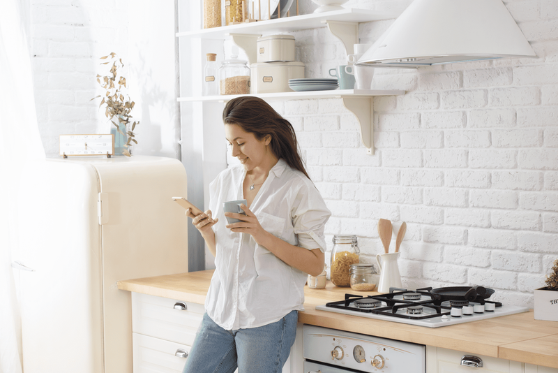 seorang wanita tersenyum berdiri di dapur dan mengancingkan telepon