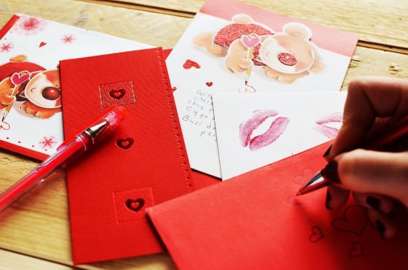Mão de mulher escrevendo carta de amor em papel vermelho