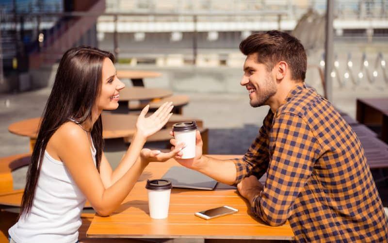 Feliz casal jovem sentado em uma mesa na frente um do outro e conversando enquanto bebe café