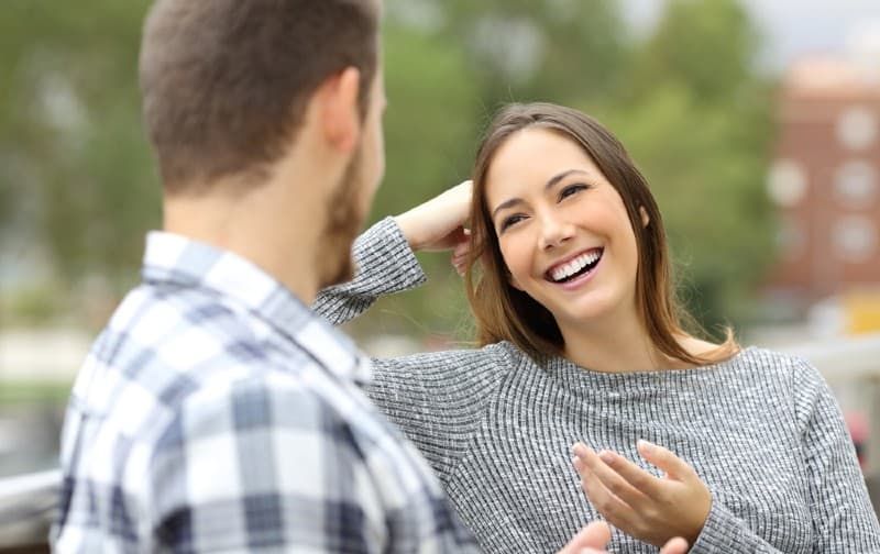 Jovem mulher sorridente falando com o homem enquanto está sentado ao lado dele ao ar livre