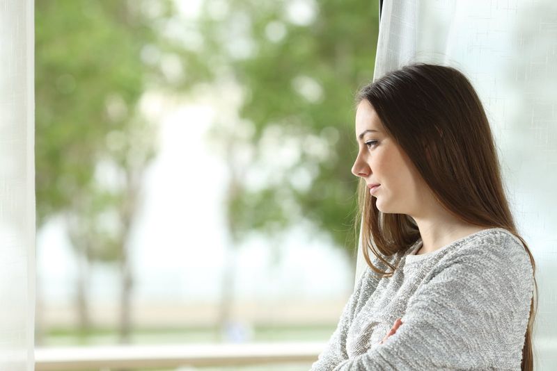 người phụ nữ trẻ lo lắng đứng bên cửa sổ